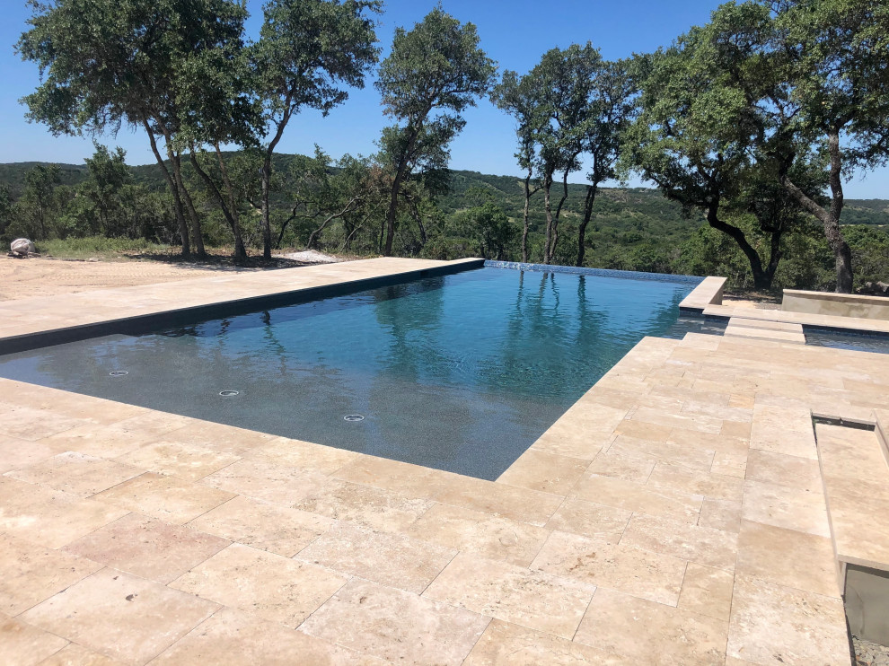 Esempio di un'ampia piscina a sfioro infinito moderna rettangolare dietro casa con una vasca idromassaggio e pedane