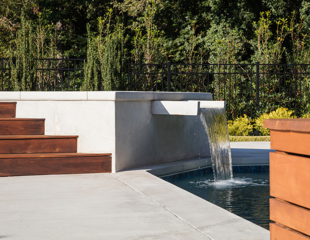 Modelo de casa de la piscina y piscina moderna grande rectangular en patio trasero con suelo de hormigón estampado