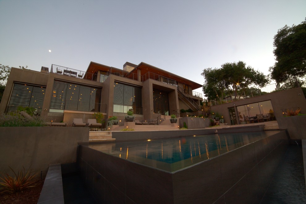 Foto di una grande piscina a sfioro infinito minimalista rettangolare dietro casa con una dépendance a bordo piscina e piastrelle