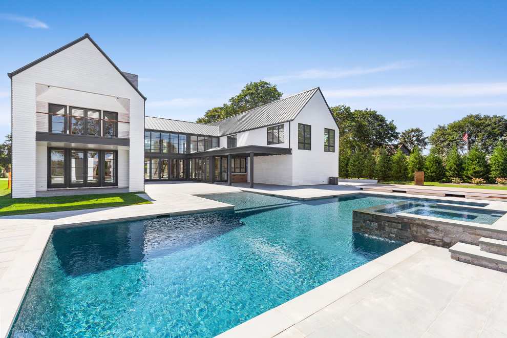 Foto di un'ampia piscina a sfioro infinito contemporanea personalizzata dietro casa con una vasca idromassaggio e pavimentazioni in pietra naturale