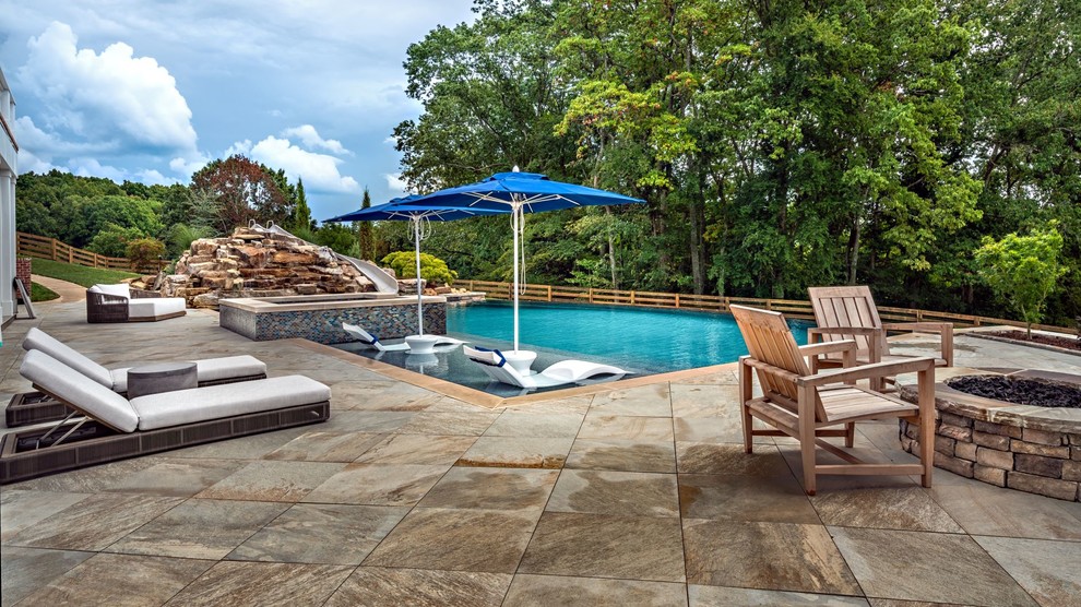 Imagen de piscina con tobogán infinita campestre extra grande a medida en patio trasero con adoquines de hormigón