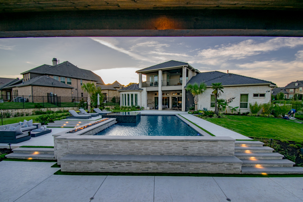 Diseño de piscina con fuente infinita minimalista grande a medida en patio trasero con suelo de hormigón estampado
