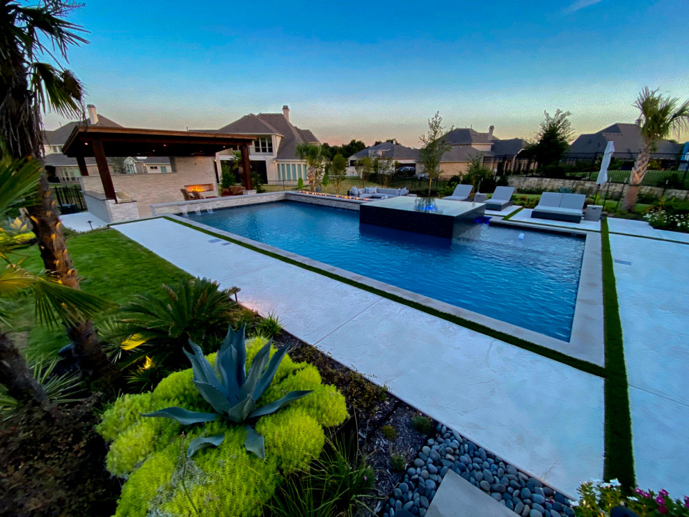 Esempio di una grande piscina a sfioro infinito minimalista personalizzata dietro casa con fontane e cemento stampato