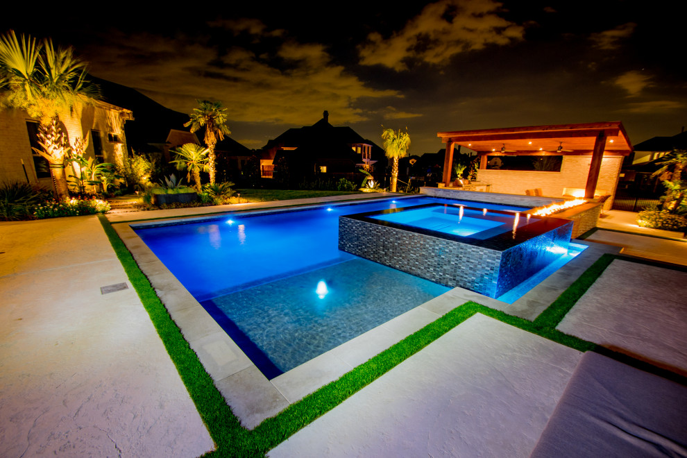 Exemple d'une grande piscine à débordement et arrière moderne sur mesure avec un point d'eau et du béton estampé.