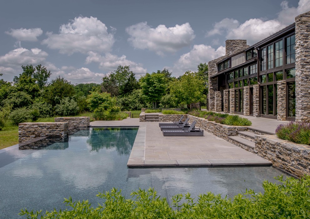 Ispirazione per una grande piscina a sfioro infinito design a "L" dietro casa con pavimentazioni in pietra naturale