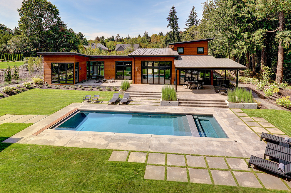 Modelo de casa de la piscina y piscina alargada actual grande rectangular en patio trasero con adoquines de hormigón