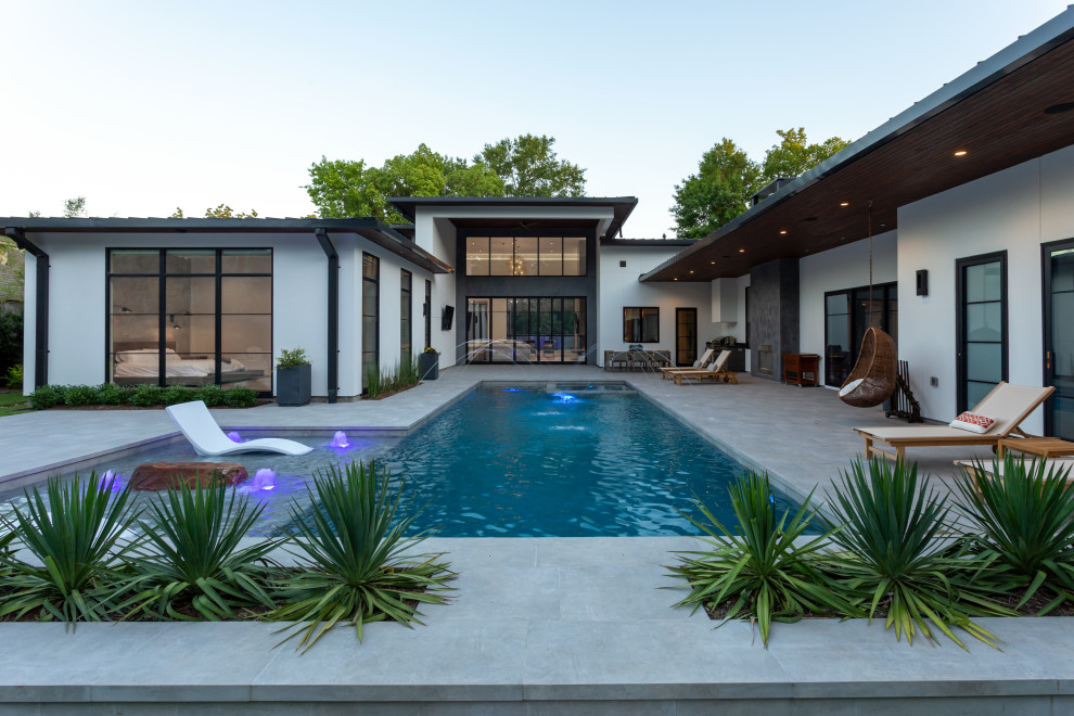 Diseño de piscina alargada moderna grande rectangular en patio trasero con paisajismo de piscina y adoquines de hormigón