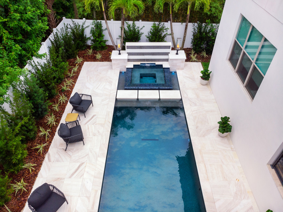 Modelo de piscina infinita actual de tamaño medio a medida en patio trasero con paisajismo de piscina y suelo de baldosas
