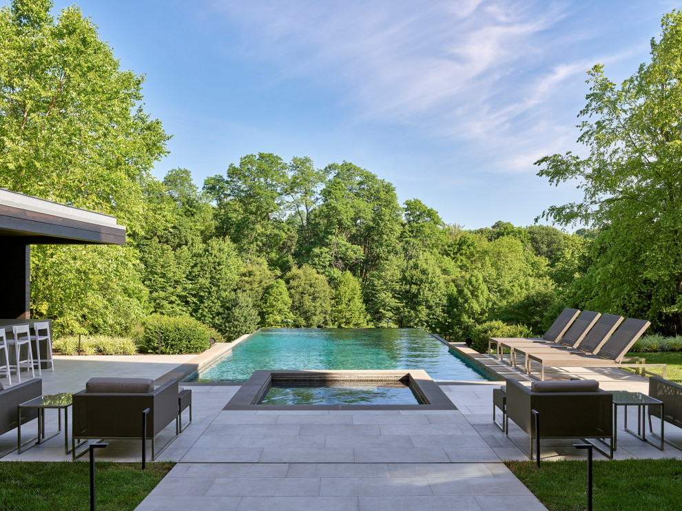 This is an example of a medium sized contemporary rectangular infinity swimming pool in Philadelphia with tiled flooring.