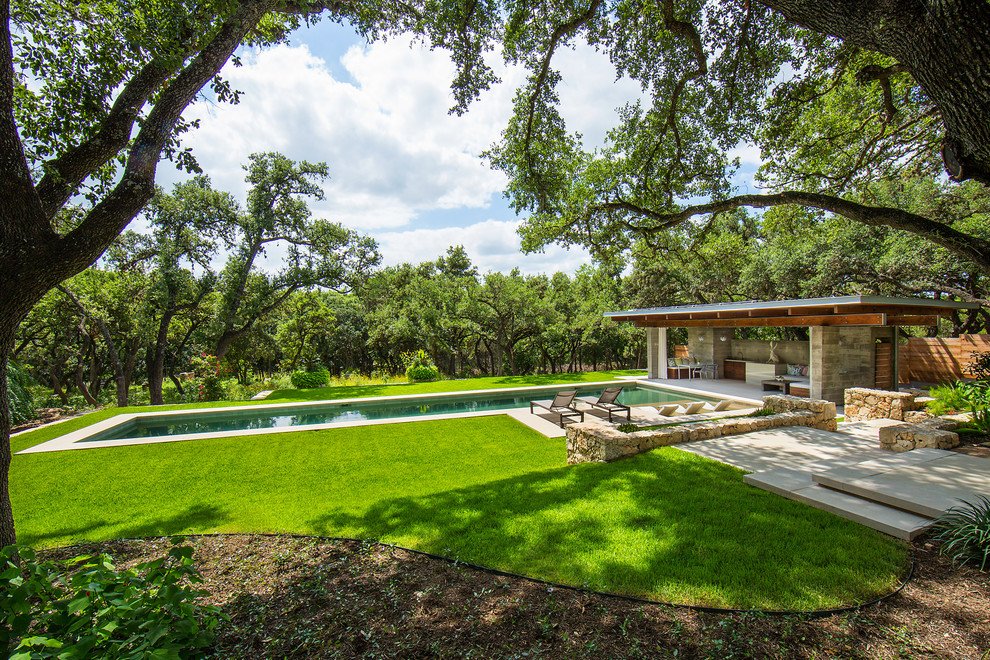 This is an example of a large modern back rectangular lengths swimming pool in Austin with a pool house and natural stone paving.
