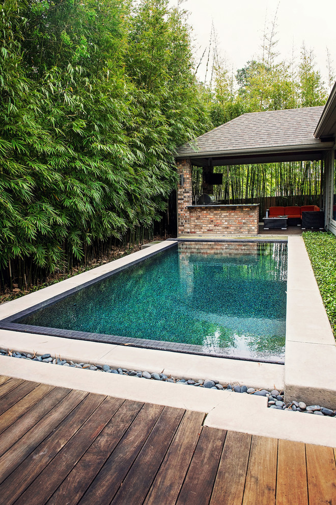 Large minimalist backyard rectangular infinity pool fountain photo in Houston with decking