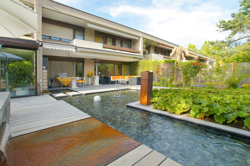 Imagen de piscina con fuente actual de tamaño medio en forma de L en patio trasero con entablado