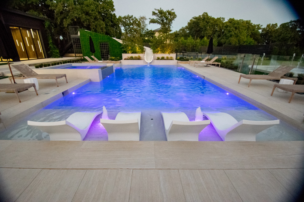 Imagen de piscina con tobogán alargada minimalista grande a medida en patio trasero con suelo de baldosas