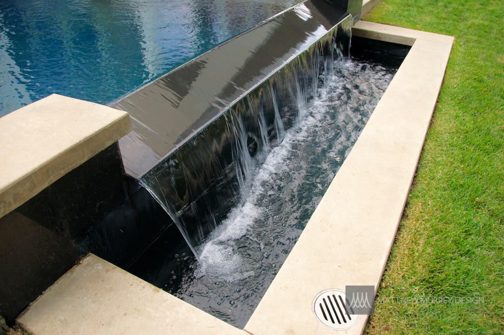 Immagine di una piscina a sfioro infinito minimalista rettangolare di medie dimensioni e dietro casa con fontane e lastre di cemento