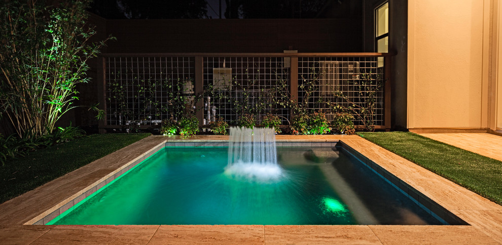 Foto de piscina con fuente actual pequeña rectangular en patio trasero con adoquines de piedra natural