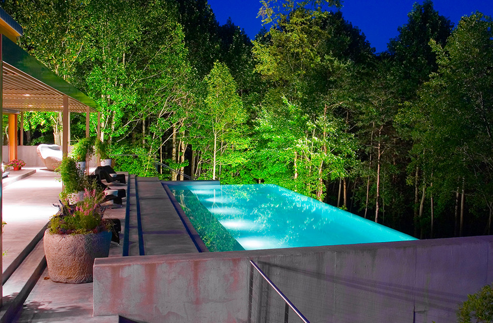 Immagine di una grande piscina a sfioro infinito minimalista rettangolare dietro casa con una dépendance a bordo piscina e lastre di cemento