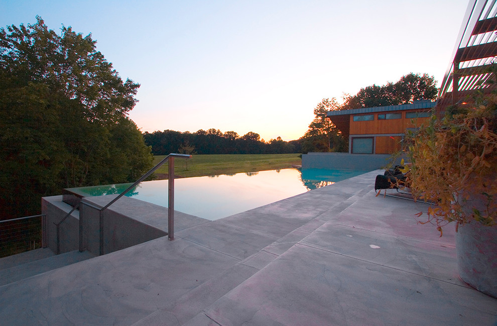 Ejemplo de casa de la piscina y piscina infinita moderna grande rectangular en patio trasero con losas de hormigón