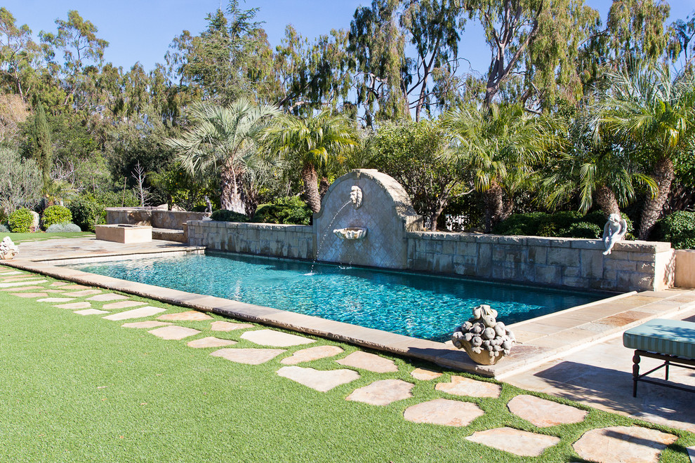 Immagine di una piscina naturale mediterranea rettangolare di medie dimensioni e dietro casa con fontane e pavimentazioni in pietra naturale
