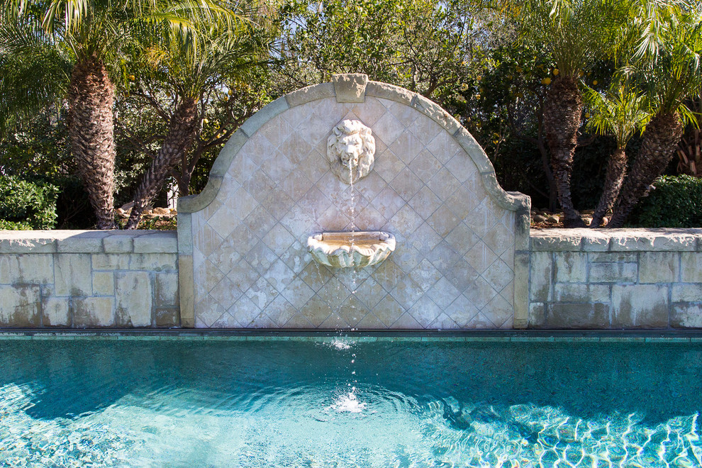 This is an example of a medium sized mediterranean back rectangular natural swimming pool in Los Angeles with a water feature and natural stone paving.