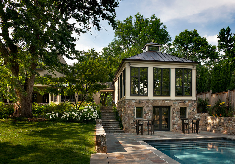 Back rectangular swimming pool in DC Metro with a pool house and natural stone paving.