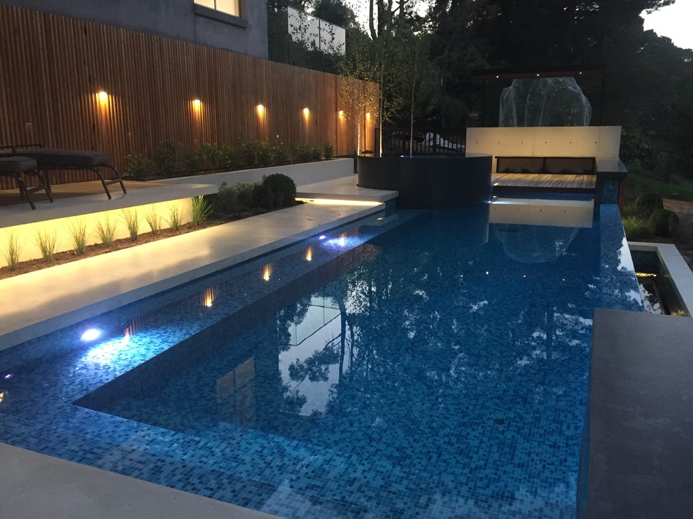 Idee per una grande piscina a sfioro infinito design personalizzata dietro casa con una vasca idromassaggio e lastre di cemento