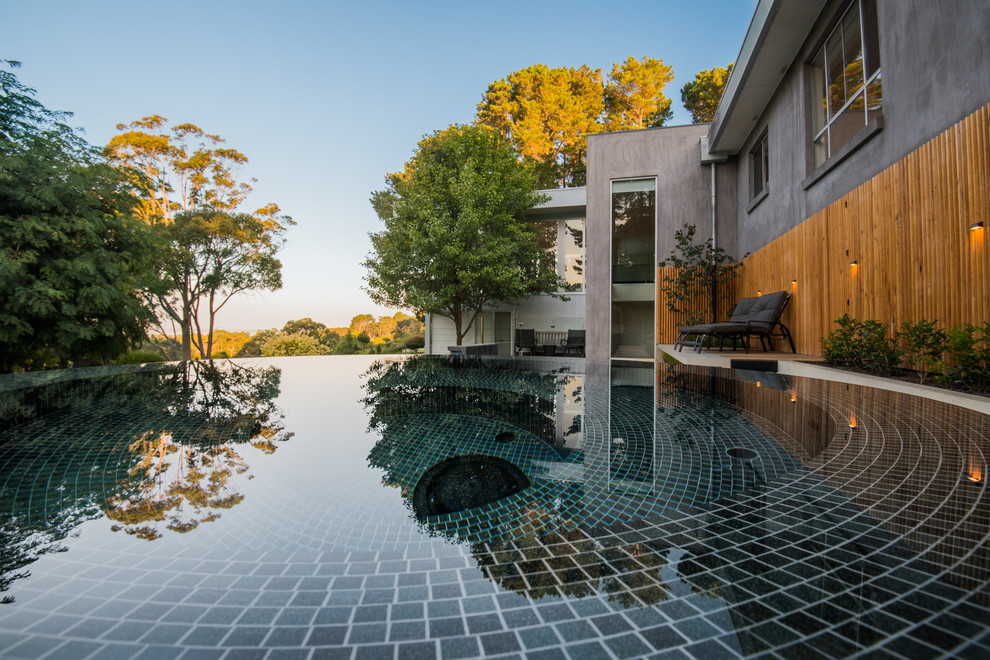 Ispirazione per una grande piscina a sfioro infinito minimal personalizzata dietro casa con una vasca idromassaggio e lastre di cemento