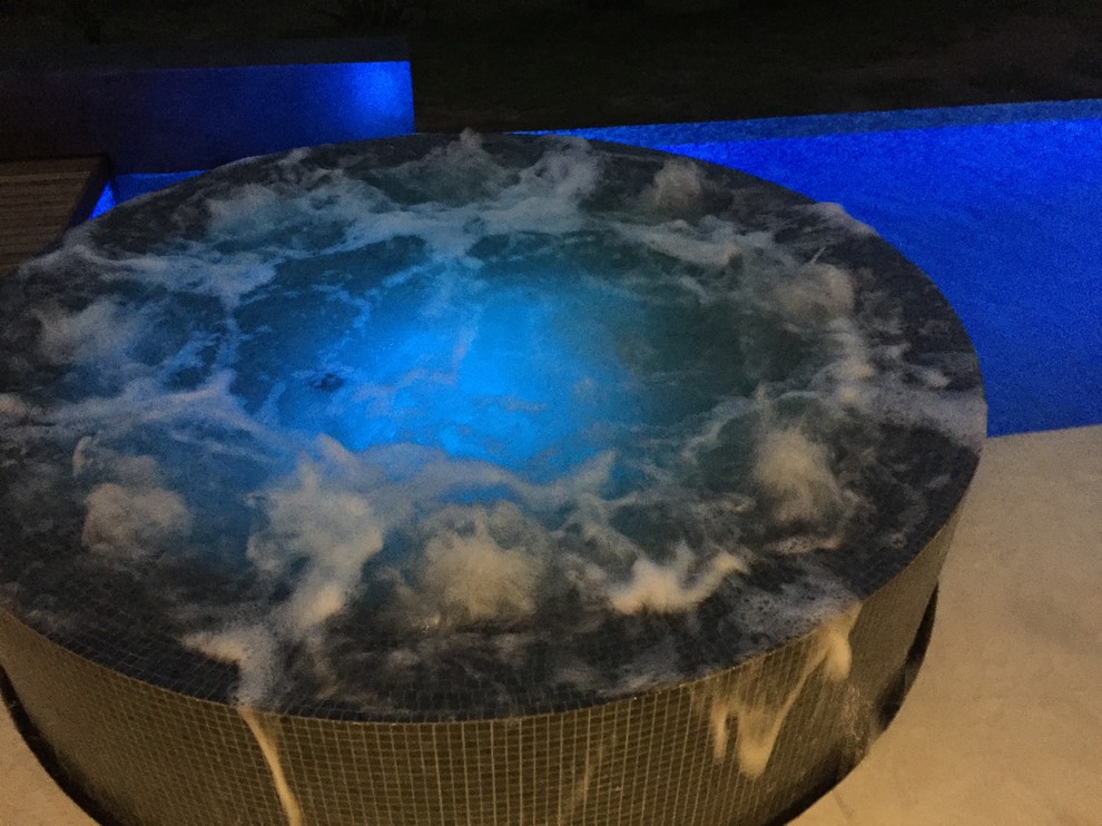 Ispirazione per una grande piscina a sfioro infinito design personalizzata dietro casa con una vasca idromassaggio e lastre di cemento