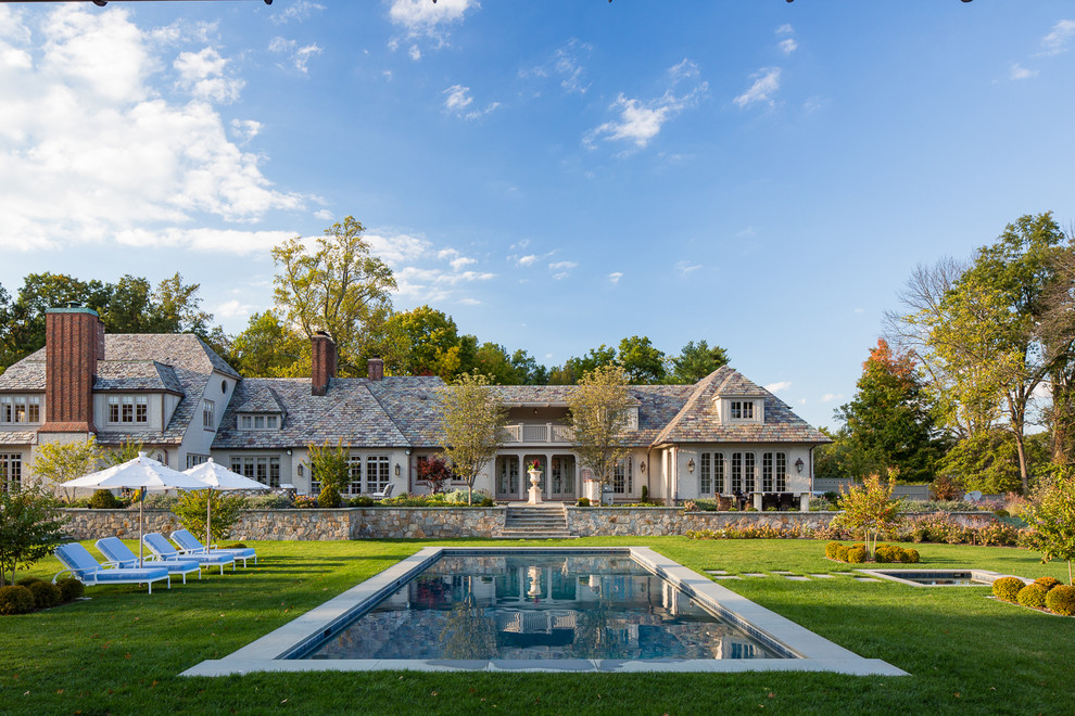 На фото: большой прямоугольный бассейн на заднем дворе в классическом стиле с джакузи и покрытием из каменной брусчатки