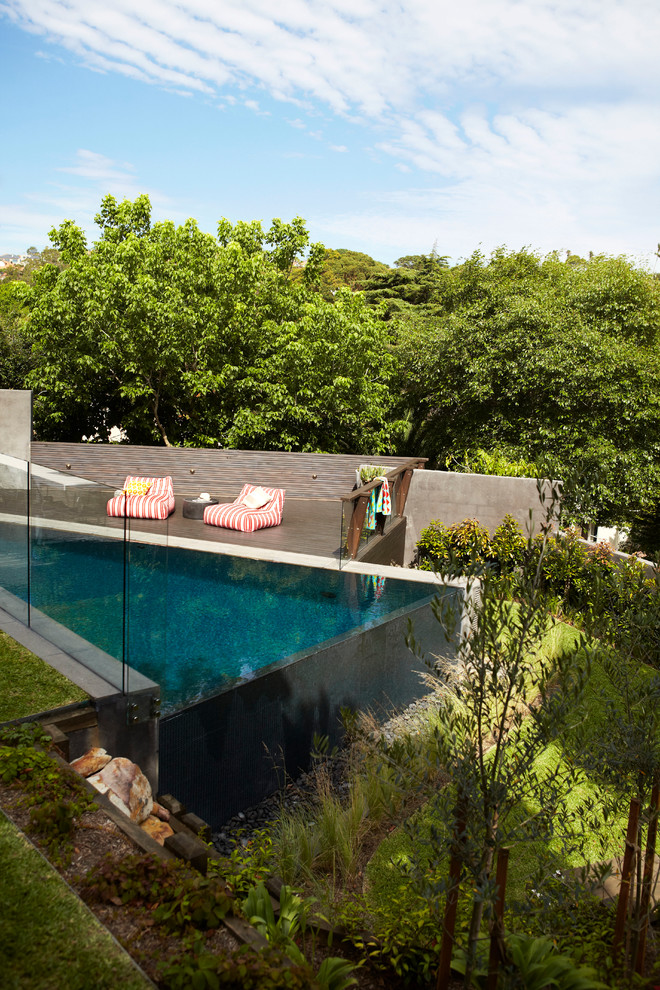 This is an example of a large contemporary back rectangular infinity swimming pool in Sydney with decking.