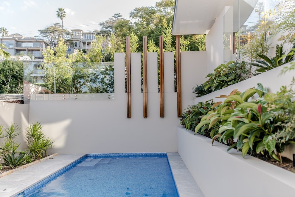 Imagen de piscina alargada actual rectangular en patio trasero con adoquines de piedra natural