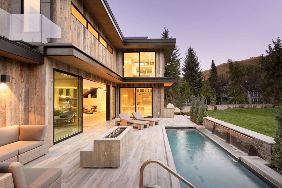Diseño de piscina con fuente alargada rústica grande rectangular en patio trasero con suelo de baldosas