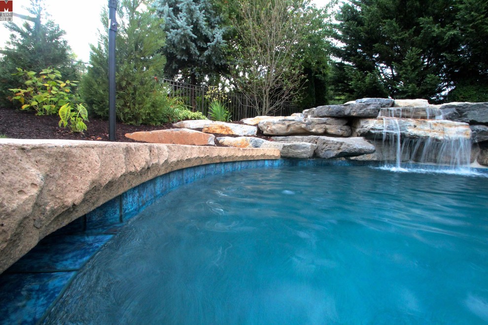 Large contemporary back custom shaped swimming pool in Philadelphia with a water feature and stamped concrete.