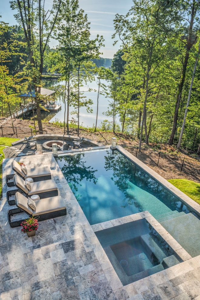 Photo of a large rustic back rectangular infinity hot tub in Charlotte with natural stone paving.