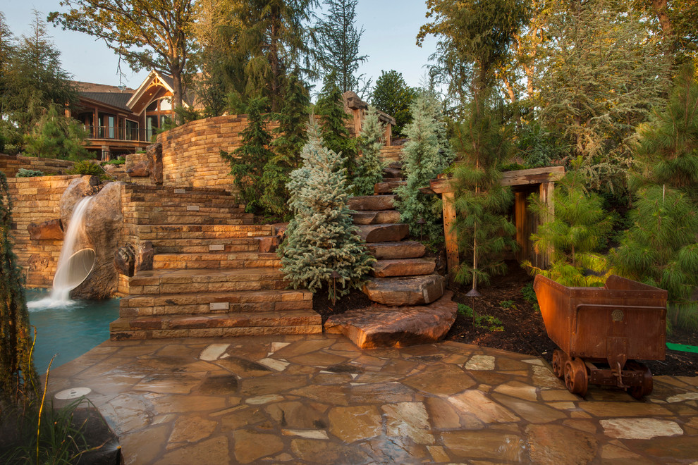 Photo of an expansive rustic back custom shaped natural swimming pool in Oklahoma City with a water feature and natural stone paving.