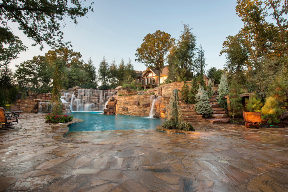 Expansive rustic back custom shaped natural swimming pool in Oklahoma City with a water slide and natural stone paving.