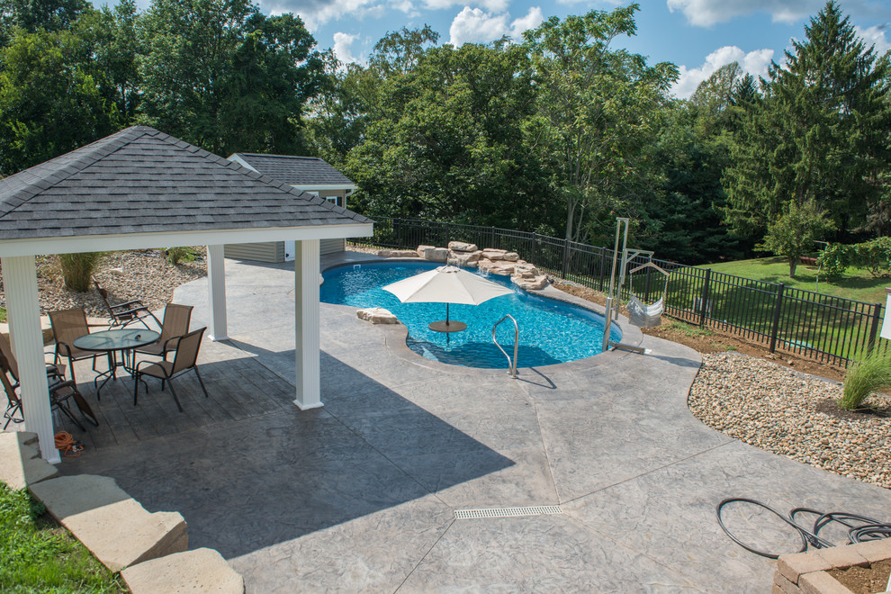 Diseño de piscina con fuente natural romántica de tamaño medio a medida en patio trasero con suelo de hormigón estampado