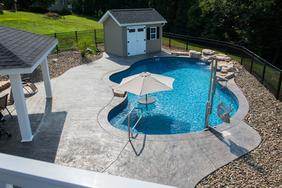 Medium sized vintage back custom shaped natural swimming pool in Other with a water feature and stamped concrete.