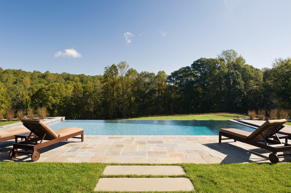 Cette photo montre une grande piscine à débordement et arrière montagne rectangle avec des pavés en pierre naturelle.