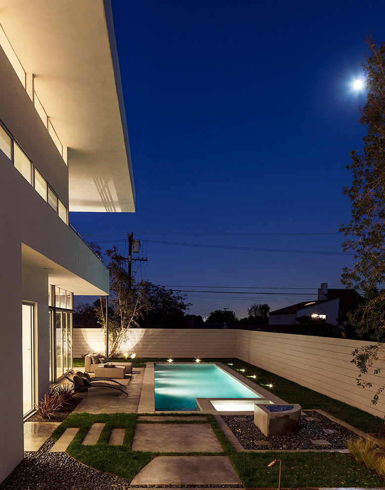 Diseño de piscina alargada actual de tamaño medio rectangular en patio trasero con adoquines de hormigón