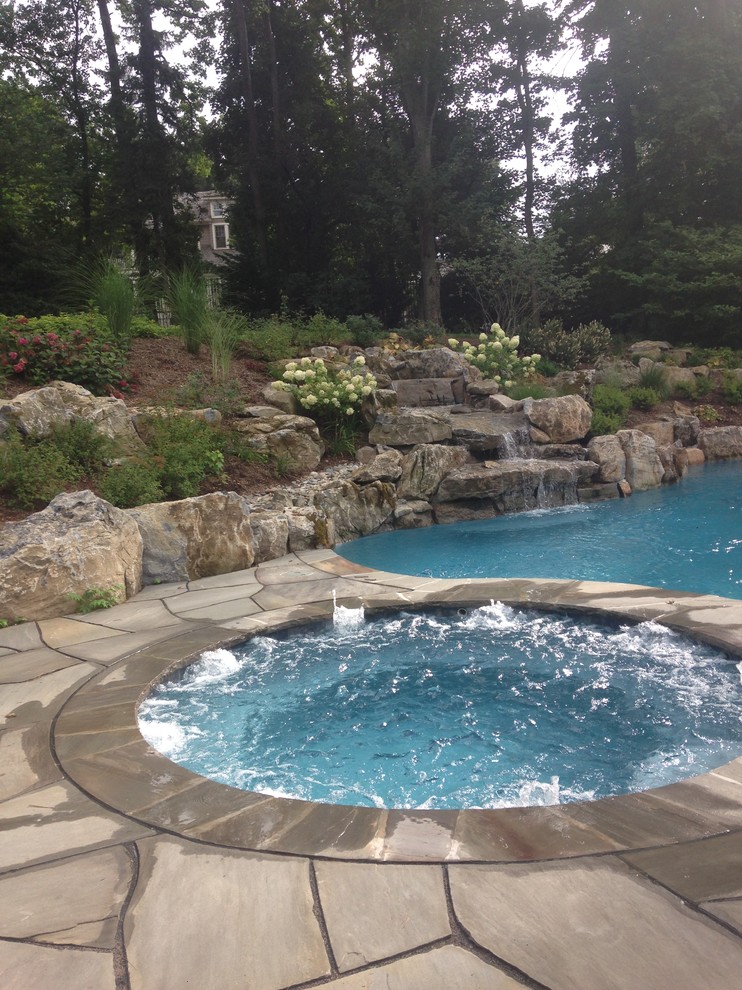 Immagine di una grande piscina naturale rustica personalizzata dietro casa con fontane e pavimentazioni in pietra naturale