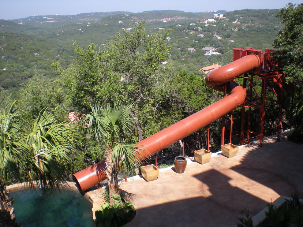 Immagine di una grande piscina naturale tropicale personalizzata dietro casa con un acquascivolo e lastre di cemento