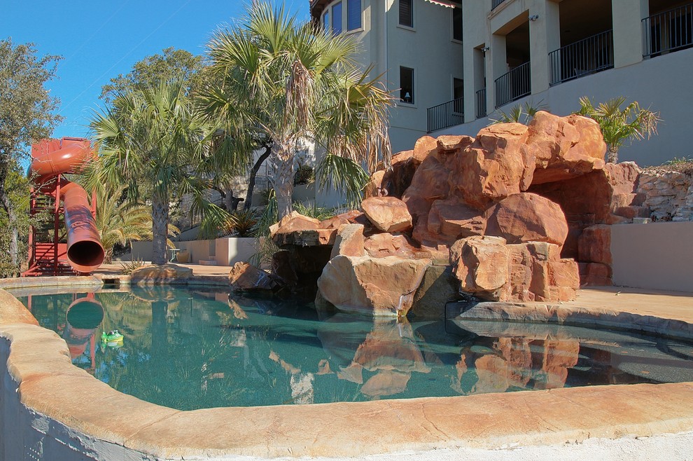 Foto di una grande piscina naturale tropicale personalizzata dietro casa con un acquascivolo e lastre di cemento
