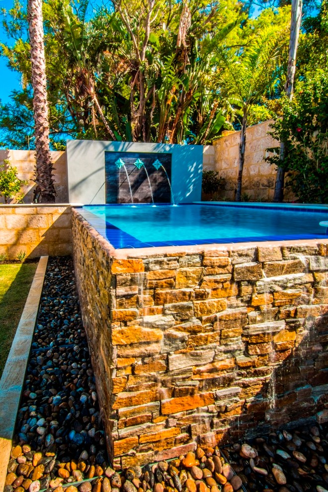 Modelo de piscina con fuente infinita clásica grande en forma de L en patio trasero con adoquines de piedra natural