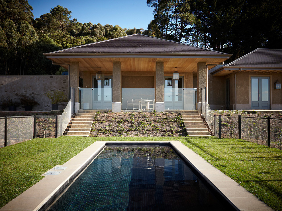 Modelo de piscina alargada de estilo de casa de campo de tamaño medio a medida en patio trasero con adoquines de piedra natural