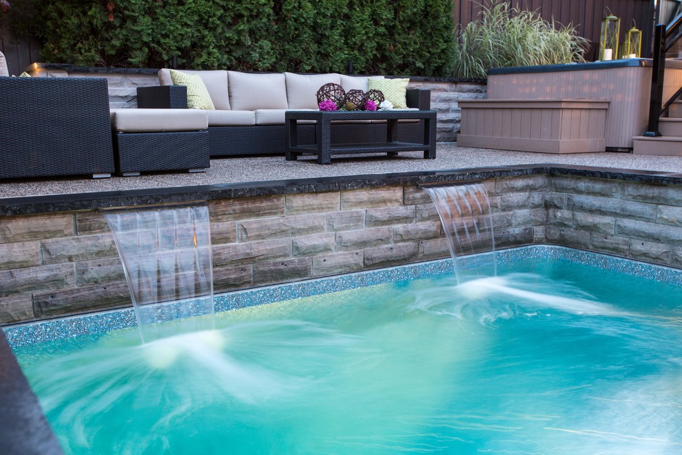 This is an example of a contemporary back swimming pool in Toronto with a water feature and natural stone paving.