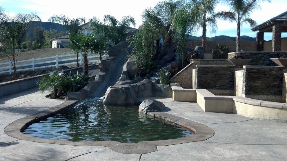Imagen de piscina con tobogán infinita exótica grande a medida en patio trasero con adoquines de piedra natural