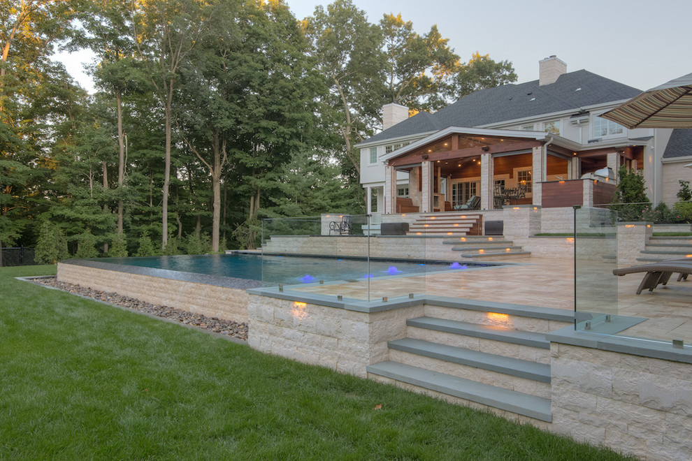 Стильный дизайн: большой прямоугольный бассейн-инфинити на заднем дворе с джакузи и покрытием из каменной брусчатки - последний тренд