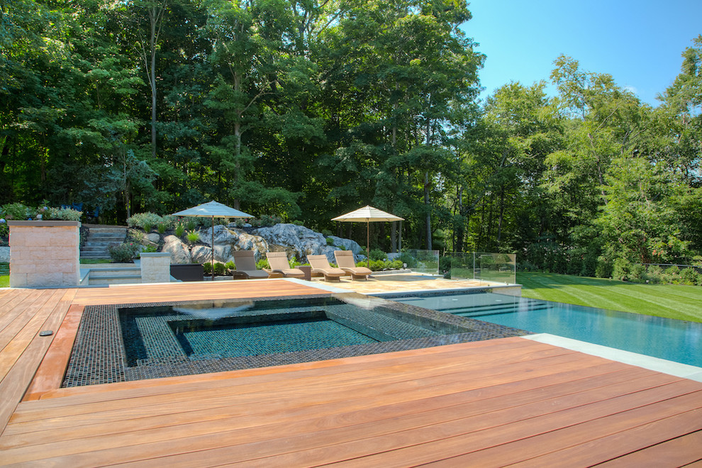 Ispirazione per una grande piscina a sfioro infinito rettangolare dietro casa con una vasca idromassaggio e pavimentazioni in pietra naturale