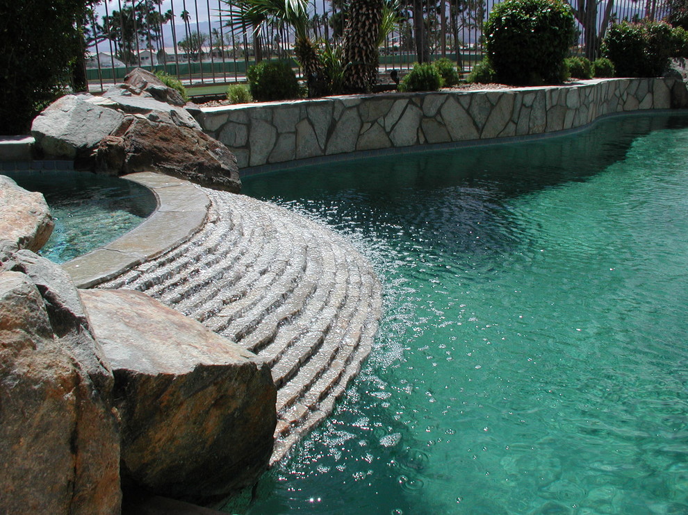Photo of a large world-inspired back custom shaped lengths hot tub in Orange County with natural stone paving.