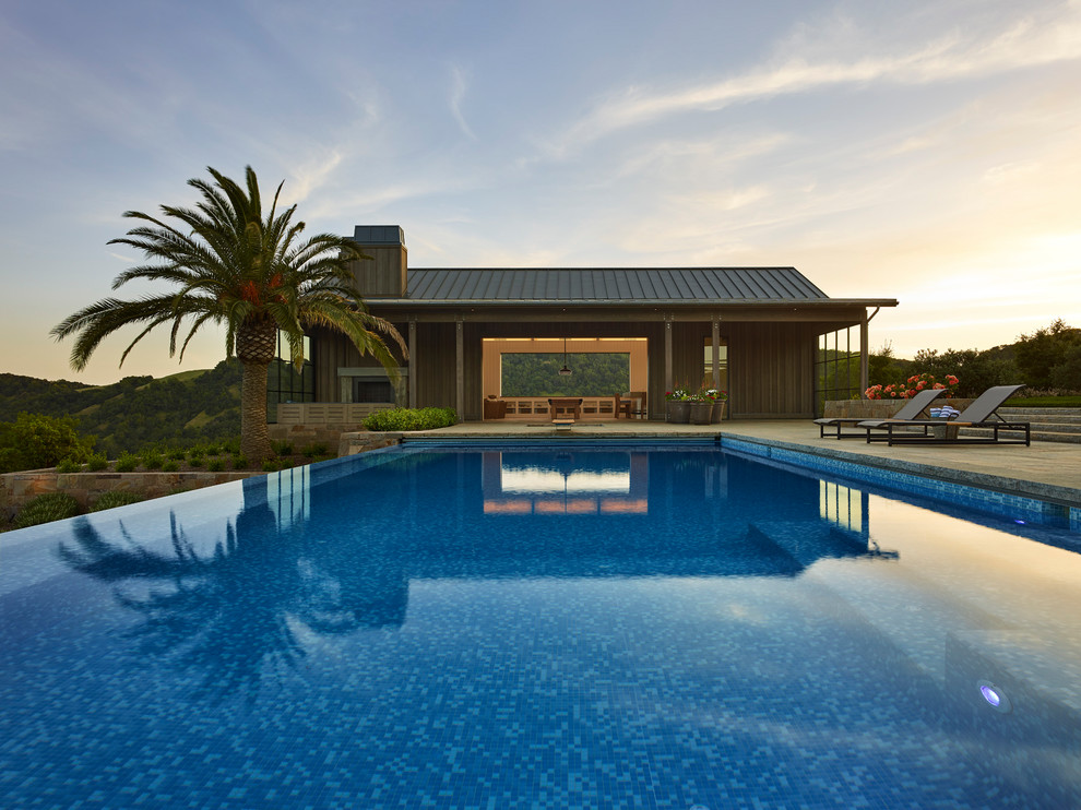 Expansive farmhouse back rectangular infinity swimming pool in San Francisco with a pool house and natural stone paving.